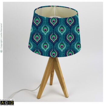 Home Decor Designs 2 Lampshade design by Lisette Niemand featuring Peacock Indulgence from the Bohemian Spirit Collection, shown in a home decor mock-up. Features repeating peacock feather motifs in rich teal, green, and magenta tones.