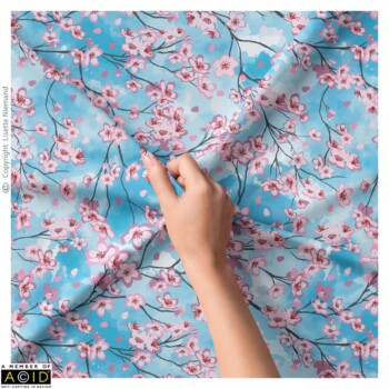 Fabric Designs 4 Fabric design by Lisette Niemand called Lying Under the Cherry Blossom Sky, shown in a textile mock-up. Features flowing cherry blossom branches with scattered petals on a soft blue background.
