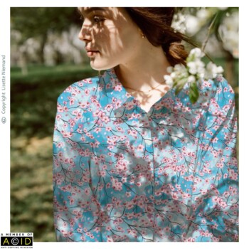 Fashion & Accessory Designs 4 Women’s blouse design by Lisette Niemand featuring Lying Under the Cherry Blossom Sky, shown in a fashion mock-up. Features soft cherry blossom branches and scattered petals on a blue cloud-like background.