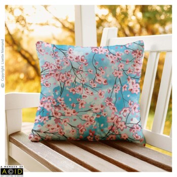 Home Decor Designs 4 Cushion design by Lisette Niemand featuring Lying Under the Cherry Blossom Sky, shown in a home decor mock-up. Features soft cherry blossom branches and petals on a blue background.